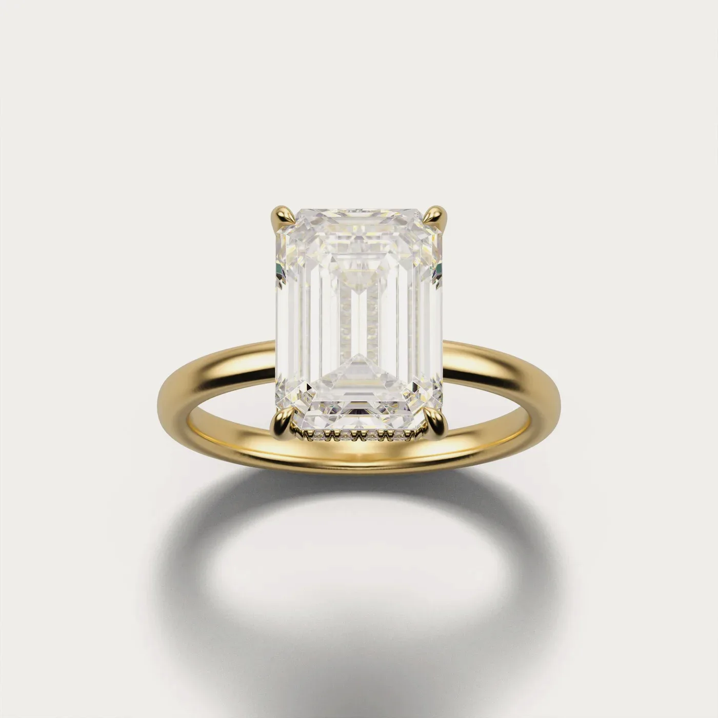 An emerald cut with a hidden halo in yellow gold, lit and photographed identically to the other two